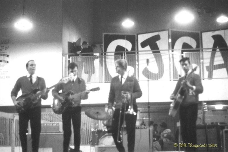 Black and White photo of a 4 piece rock band from 1963. CJCA is in large letters in the back