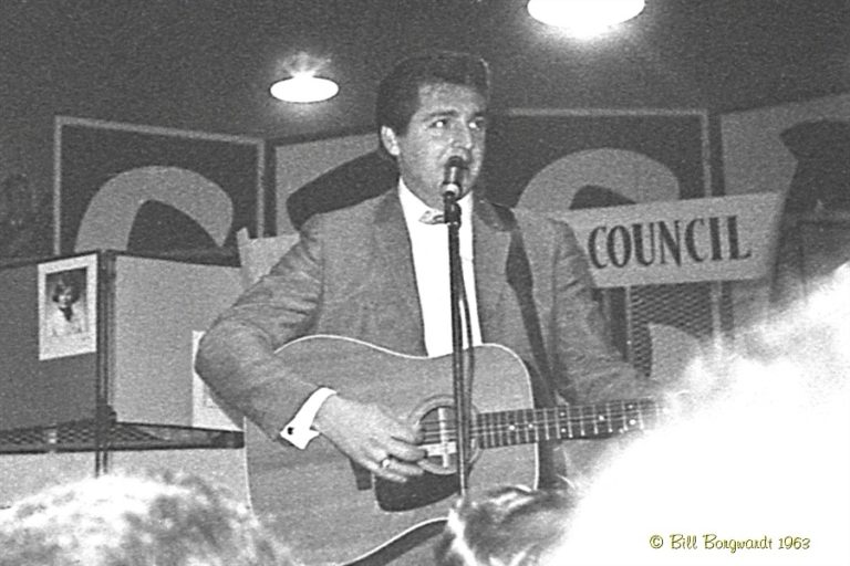 Black and White photo, 1963, of man signing with an acoustic guitar