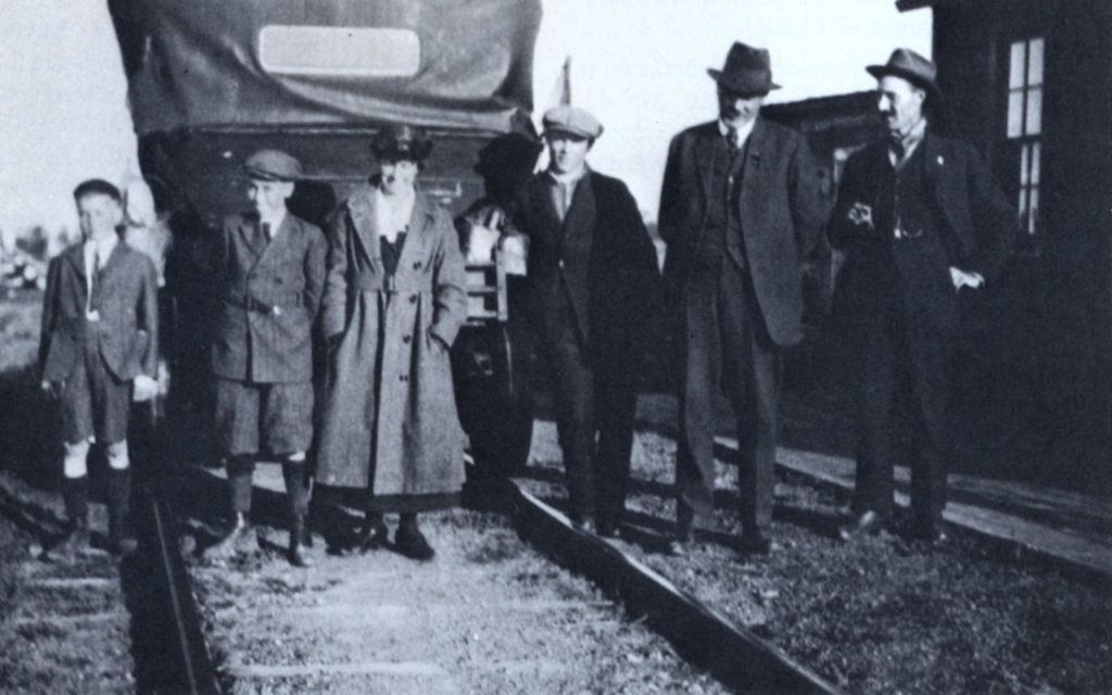 B&W photo of the Côté family and railway employees in front of a car outfitted to go on the railroad tracks, circa 1922.